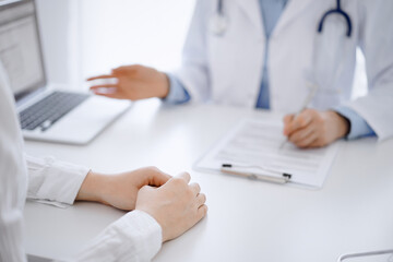 Doctor and patient using tablet computer while sitting opposite each other at the desk in clinic. The focus is on female hands near physician, close up. Medicine concept