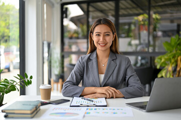 Attractive Asian businesswoman or female boss in formal business suit sits at her desk