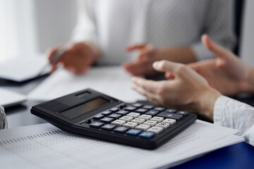 Woman accountant using a pen and laptop computer while counting and discussing taxes with a client, focus on the calculator. Business audit and finance concepts