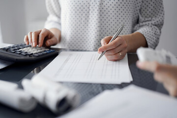 Woman accountant using a calculator and laptop computer while counting taxes for a client. Business...