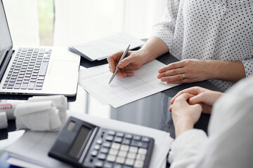 Woman accountant using a calculator and laptop computer while counting taxes for a client. Business...