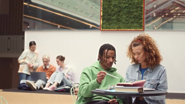 Slowmo of multiethnic couple of first year college students studying together sitting at table indoors in college
