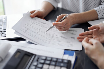 Female accountant pointing with a pen into audit paper while explaining tax counting results, close...