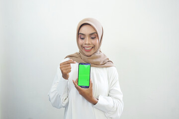 Excited beautiful Asian muslim woman showing green screen mobile phone isolated over white background.