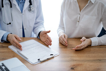 Doctor and patient discussing something while sitting near each other at the wooden desk in clinic, view from above. Medicine concept