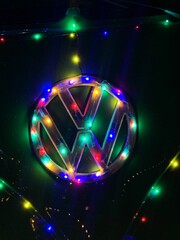Obraz premium Vertical closeup of the Volkswagen logo on the vehicle surrounded with colorful Christmas lights