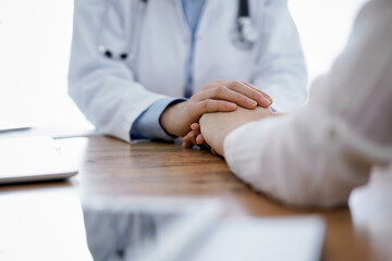 Doctor and patient sitting at the wooden table in clinic. Female physician's hands reassuring woman. Medicine concept