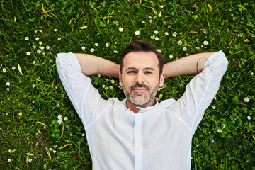 Handsome adult man lying down on grass with daisies
