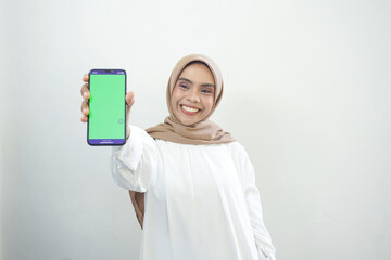 Excited beautiful Asian muslim woman showing green screen mobile phone isolated over white background.