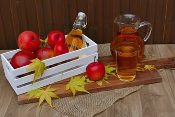 Glas und Karaffe mit Apfelsaft mit roten Äpfeln auf Holztisch.