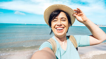 Happy senior woman taking selfie with smart mobile phone at the beach - Older female enjoying summer vacation - Summertime holidays, mature people and traveling concept - Powered by Adobe