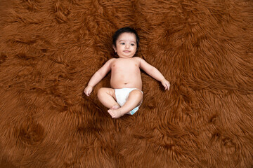 Cute little indian baby wearing diaper lying on brown fur background. Asian two months old newborn baby.