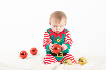 baby in elf costume grabbing christmas balls with serious expression