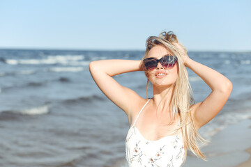 Happy blonde woman in free happiness bliss on ocean beach standing with sun glasses and posing