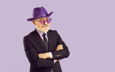 Portrait of happy confident handsome senior man in classic suit, purple fedora hat and purple...