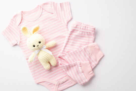 Baby shower concept. Top view photo of pink infant clothes bodysuit pants and knitted rabbit toy on isolated white background
