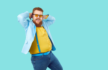 Funny redhead Caucasian man with beard and mustache emotionally performs fashion dance demonstrating emancipation and self-confidence dressed in stylish big size clothes stands in turquoise studio