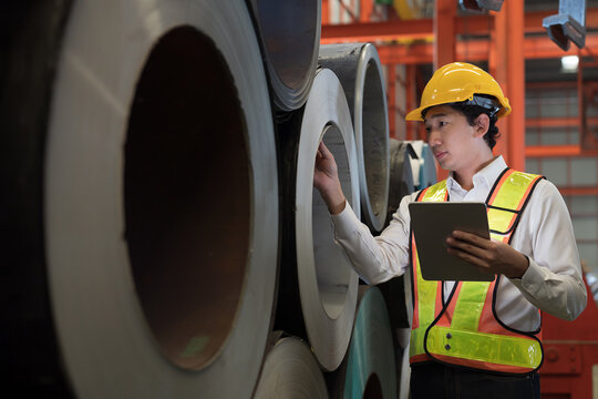 Asian male factory worker inspecting quality rolls of galvanized or metal sheet in factory. Asian male worker working in warehouse of raw materials. Metalwork during manufacturing process in plant - Powered by Adobe