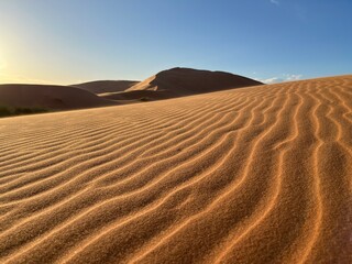 Fototapeta na wymiar Dunes in the Sahara desert, Merzouga desert, grains of sand forming small waves on the dunes, panoramic view. Setting sun. Morocco 