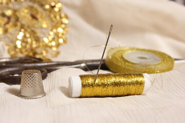 Spool of Gold Thread and Scissors With Thimble on Off White Fabric With Gold Sequins