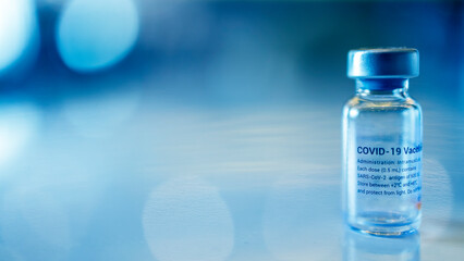 Blue tone of covid 19 vaccine on table with blur background and bokeh.Sar Cov 2 antigen for protection of corona virus pandemic.Bottle or vial of drug with medical preparation.Influenza vaccination.