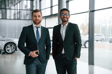 Standing and smiling. Two businessmen are working together in the car showroom