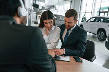 Family is buying new automobile. Three people are working together in the car showroom