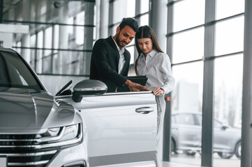 Man in formal clothes is consulting woman about the automobile in the car dealership