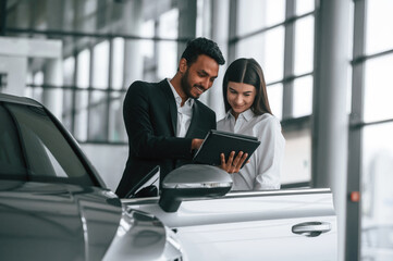 Showing information in the graphic tablet. Man in formal clothes is consulting woman about the...