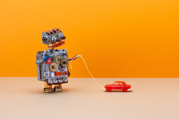 Robot game with miniature toy red car. A mechanical robot pulls a plastic automobile by a string. Range beige background, copy space.