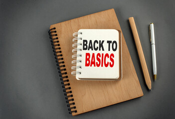 BACK TO BASICS text on notebook with pen and pencil on grey background