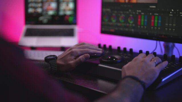 Close-up of a man's hand making edits on a special panel. Young man in glasses working on video editing on computer doing montage and color correction. Concept of creating video content.