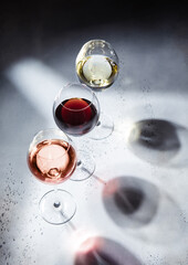 Pink rose,red and white wine glasses on light background with shadows.