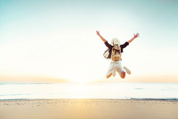 Plakat Happy traveler enjoying freedom jumping at the beach - Cheerful hiker with backpack raising hands up at sunset - Wellbeing, happiness, summer holidays and travel concept
