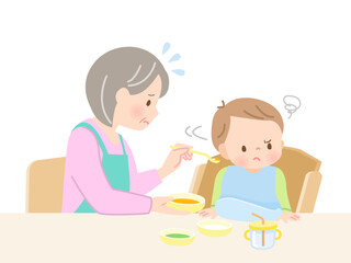 赤ちゃんに離乳食を食べさせる祖母と嫌がる赤ちゃん