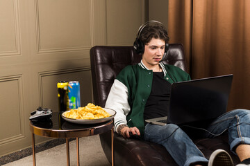 A boy or young man sitting on a couch and playing video games with a laptop while wearing...