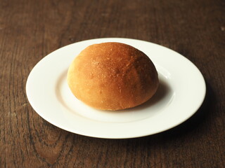 golden brown baked soft bread bun on white plate on wood
