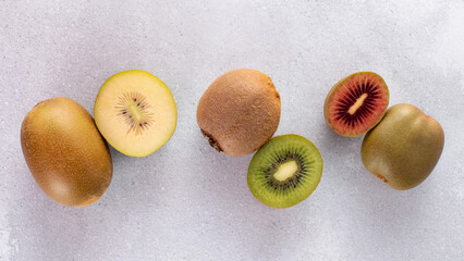 Different varieties of kiwi lie in a pile on the table. Halves of red, yellow and green kiwi. 
