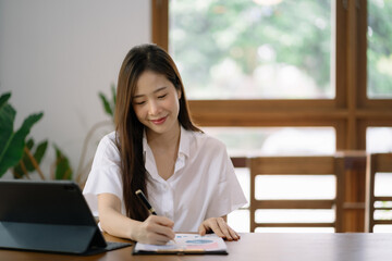 Cropped view of smiling beautiful woman writing in a journal while sitting at desk in office.