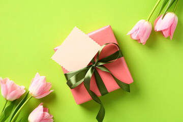 Happy Mothers Day gift with greeting card mockup and tulips on green background. Flat lay, top view, copy space.