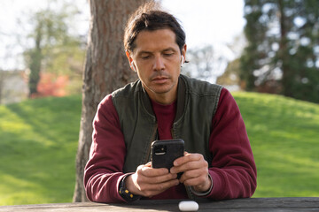 man listening to music with airpods through his mobile phone in a park during spring