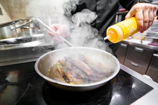 man chef cooking fried meat slice in frying pan on restaurant kitchen