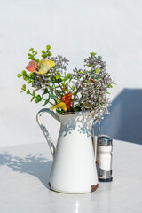 Eine alte Kanne mit Blumen und Salzstreuer auf einem Tisch