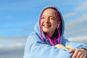 Portrait of a caucasian teenage girl with pink braids using wireless headphones against the blue...