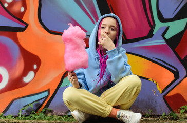 Caucasian teenage hipster girl with pink braids eats cotton candy against the background of a...