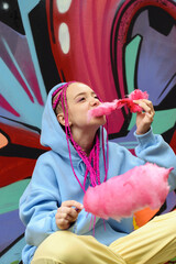 Caucasian teenage hipster girl with pink braids eats cotton candy against the background of a...