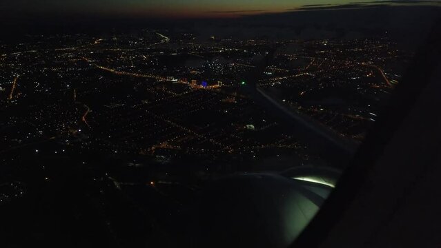 View from the plane window of the lights of a glowing city at night. Flight over the metropolis at night on an airplane view from the wing window. Aircraft takeoff and climb