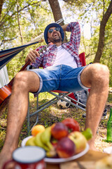 Cheerful hipster man enjoying his time in nature. Summertime camping and picnic in forest. Holiday, leisure, fun, lifestyle concept.