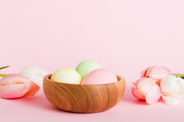 Happy Easter composition. Easter eggs in basket on colored table with yellow Tulips. Natural dyed colorful eggs background with copy space