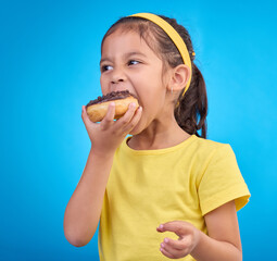 Donut, eating and sweet with girl in studio for junk food, sugar and happiness. Snack, cake and cute with face of child and dessert for candy diet and chocolate isolated on blue background